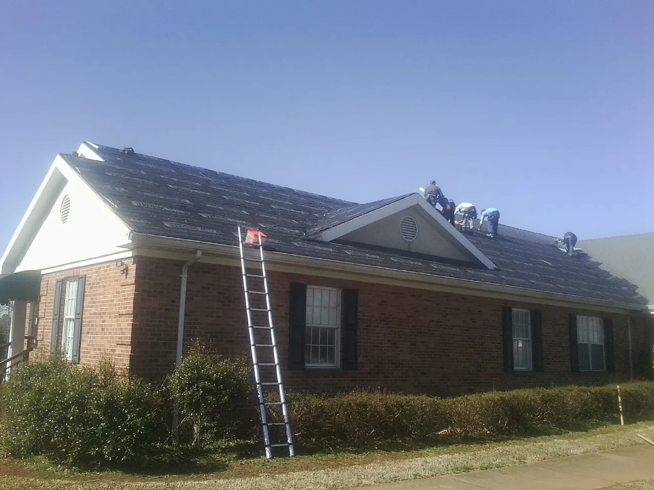 Crew tearing shingles off a brick ranch roof with a ladder set — Emergency Roof Repair work by our crew in Starr