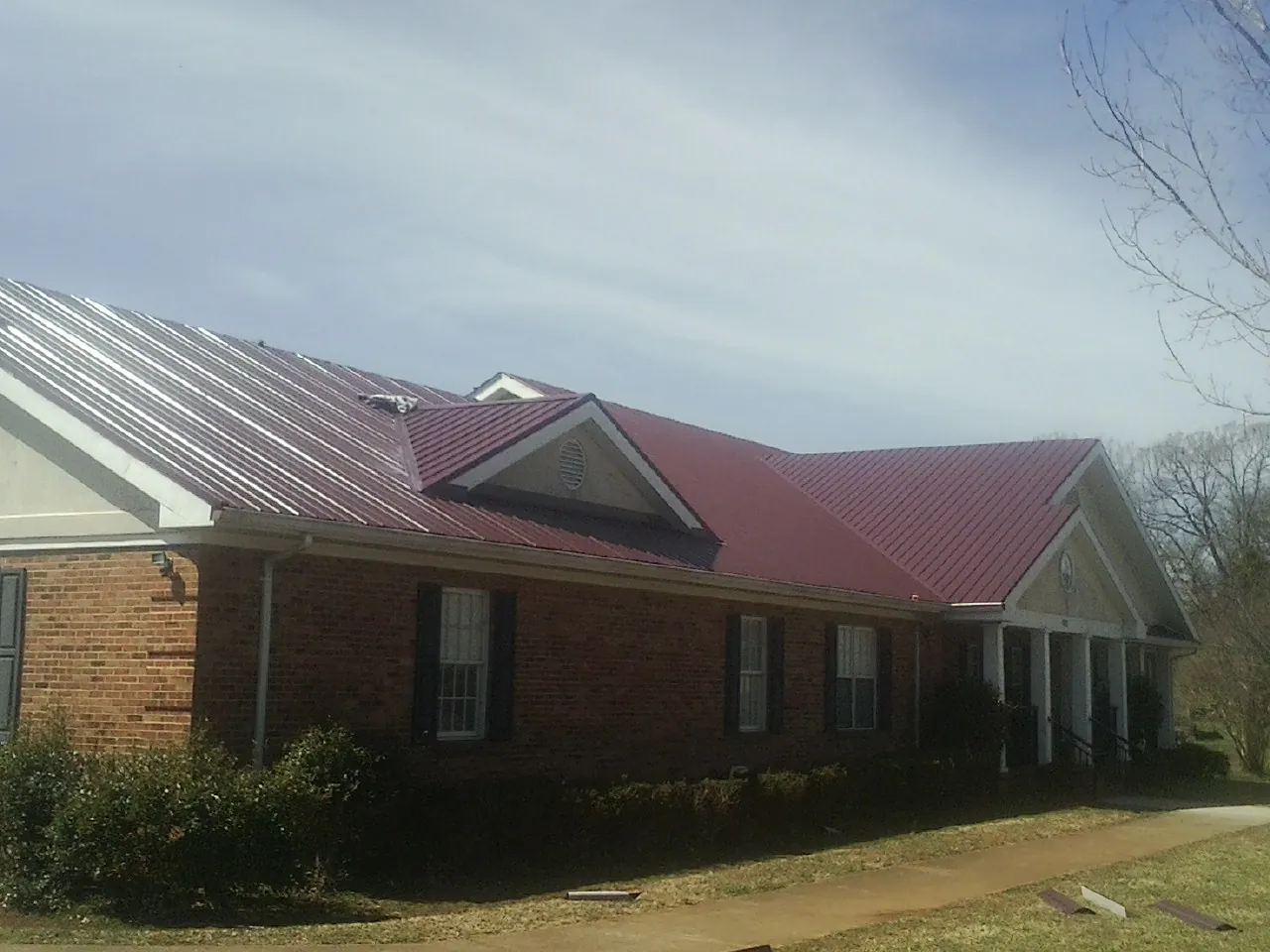 Red metal roof with gabled entries on a long brick building, from a Hail Damage Roof Repair job in Starr
