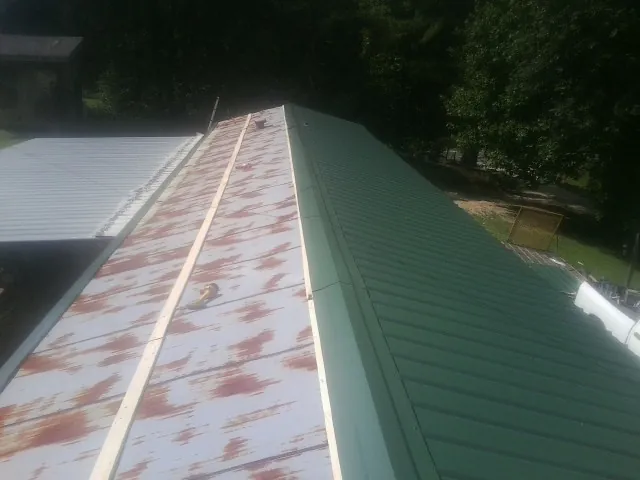 Old rusted panels beside newly installed green metal roofing — Wind Damage Roof Repair by Roofing Brothers in Starr