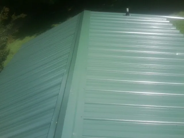 New green metal panels meeting at the ridge of a roof — Flat Roof Repair work by our crew in Starr