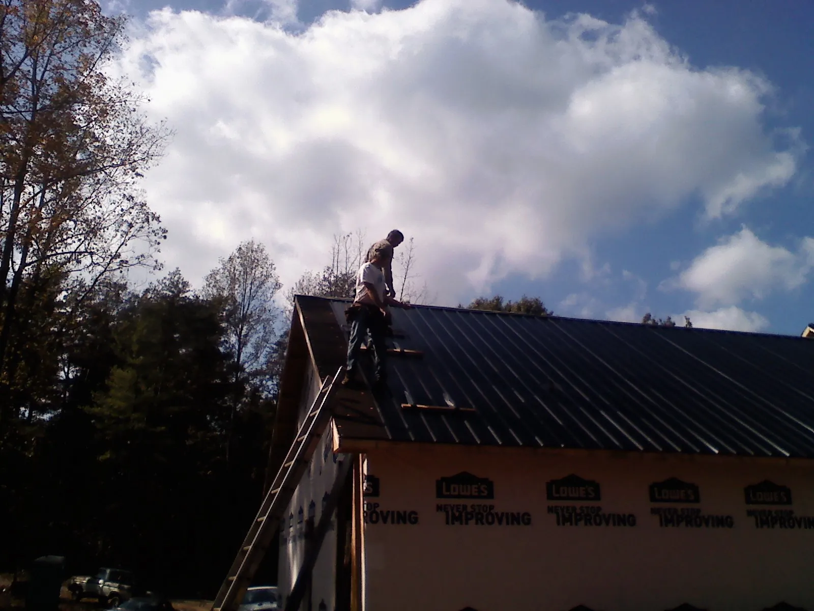 Roofer fastening dark metal panels high against a cloudy sky, from a Roof Inspection job in Starr